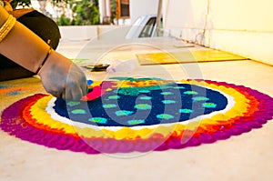 Hand of young indian girl making rangoli from colored powder on diwali eve