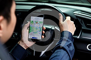 Hand of young man holding mobile phone with an open online maps app in car