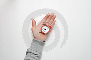 The hand of a young man holds a red alarm clock. Time, sleep, awakening concept