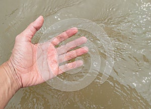 The hand of a young man is touching the flowing water