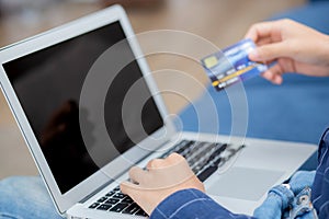 Hand of young man using laptop computer display blank screen shopping online with credit card on sofa at home.