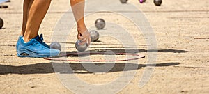 Hand of young sporty woman in sports shoes catching metal petanque ball to compete in qualifying game playing petanque game on a photo