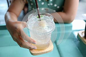 Hand of young woman holding lychee juice with soda .