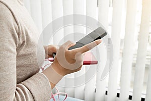 The hand of a young woman holding a smart phone and a modern backup battery charger Charge your smartphone with a backup battery,