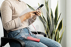 The hand of a young woman holding a smart phone and a modern spare battery charger Place the lap to charge the smartphone with a