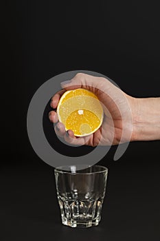 Hand of a young woman squeezes juice from an orange into a glass