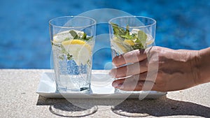 Hand of a young woman takes a glass of fresh lemon infused mineral water