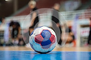 Handball ball on court` s floor. Blurred referees, coaches and athletes and field background.