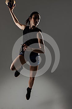 Handball player posing on gray background. Girl jumping with ball