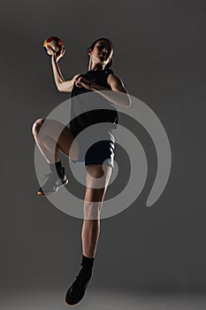 Handball player posing on gray background. Girl jumping with ball