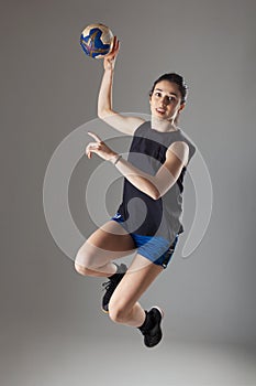 Handball player posing on light gray background. Girl jumping with ball