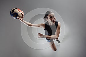 Handball player posing on light gray background. Girl jumping with ball