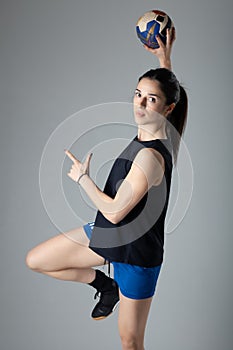 Handball player posing on light gray background. Girl jumping with ball