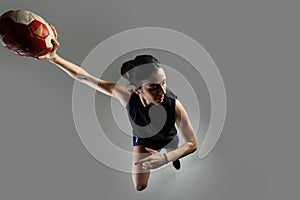 Handball player posing on light gray background. Girl jumping with ball