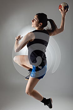 Handball player posing on light gray background. Girl jumping with ball