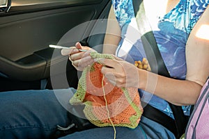 Handcraft. A girl knits in the back seat of a car