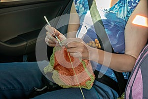 Handcraft. A girl knits in the back seat of a car