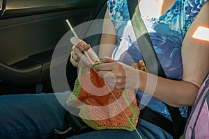 Handcraft. A girl knits in the back seat of a car