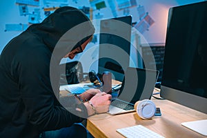 handcuffed hacker in hoodie in front of laptop