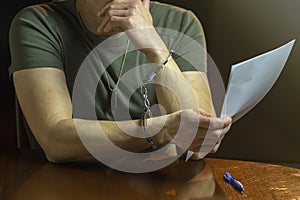 A handcuffed military man reads a document at his desk. Concept: testimony, investigation and inquiry.