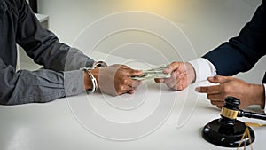 A handcuffed prisoner who has arrested a criminal with a dollar in hand who is paying the probable to keep from the photo