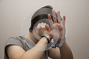 A handcuffed teenager covers his face with his hands on a gray background, medium plan. Juvenile delinquent, criminal liability of