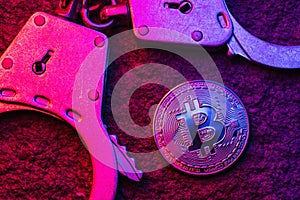 Handcuffs and bitcoin on the table, top view. Concept on the topic of fraudulent activities with digital currency