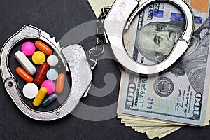 Handcuffs, drugs and us dollars banknotes on dark background suggesting punishment for prohibited substance traffic
