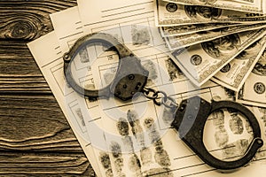 Handcuffs, fingerprints, dollars on a wooden background.