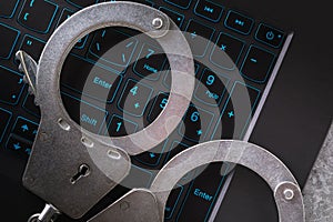 Handcuffs on a laptop keyboard, close-up. Concept on the topic of punishment for fraudulent activities in the digital space