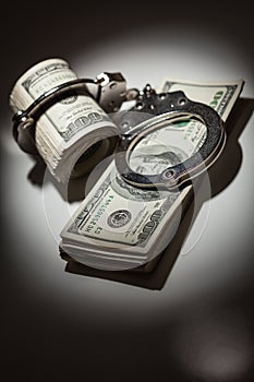 Handcuffs Locked on Roll of One Hundred Dollar Bills Under Spotlight