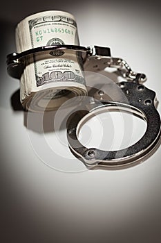 Handcuffs Locked on Roll of One Hundred Dollar Bills Under Spotlight