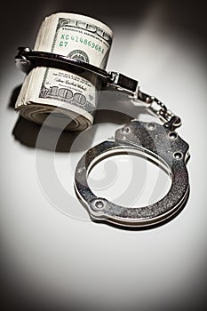 Handcuffs Locked on Roll of One Hundred Dollar Bills Under Spotlight