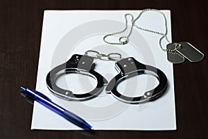 handcuffs and military badges lying on a white sheet of paper, and a blue ballpoint pen. Concept: law and justice,