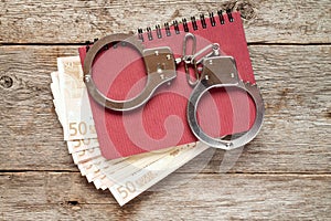 Handcuffs on notebook with euro banknotes