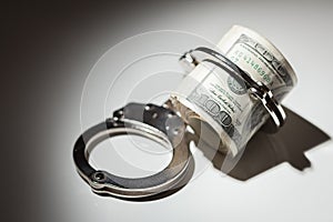 Handcuffs on Roll of One Hundred Dollar Bills Under Spotlight