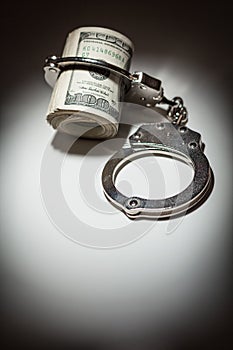 Handcuffs on Roll of One Hundred Dollar Bills Under Spotlight