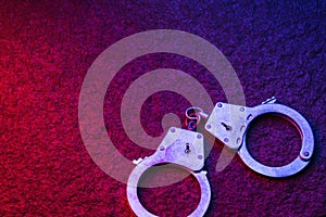 Handcuffs on a stone surface, illuminated by flashing lights of a police car with copy space