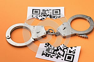 Handcuffs and a torn sheet with a barcode on a colored background, the concept of punishment for counterfeiting QR codes