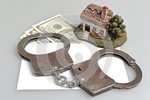 Handcuffs, toy house and white envelope with money on gray