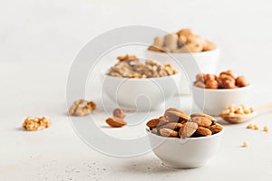 A handful of almonds in a white bowl, assorted nuts on a light background. Healthy snacks, healthy fats. Copy space