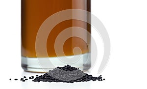 A handful of black cumin seeds on the background of a glass bottle with black seed oil.