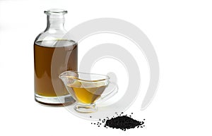 A handful of black cumin seeds and black seed oil in a glass bottle and gravy boat.