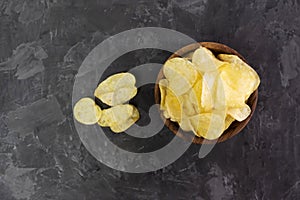 Handful of ordinary potato chips in a wooden bowl, cup on a dark background. Place for text. Beer snack. Junk food