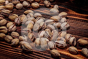 A handful of Pistachio nuts are scattered on a wooden table