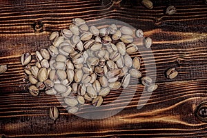 A handful of Pistachio nuts are scattered on a wooden table