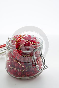 Handful of red currants in an open glass jar on a white background