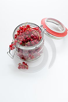 Handful of red currants in an open glass jar on a white background