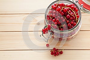 Handful of red currants in an open glass jar on a wooden background