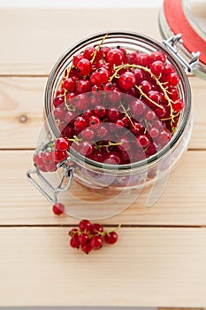 Handful of red currants in an open glass jar on a wooden background